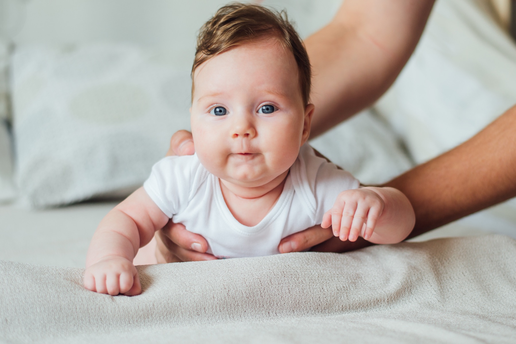 A baby in supported tummy time on a soft surface, looking up with engaged blue eyes.